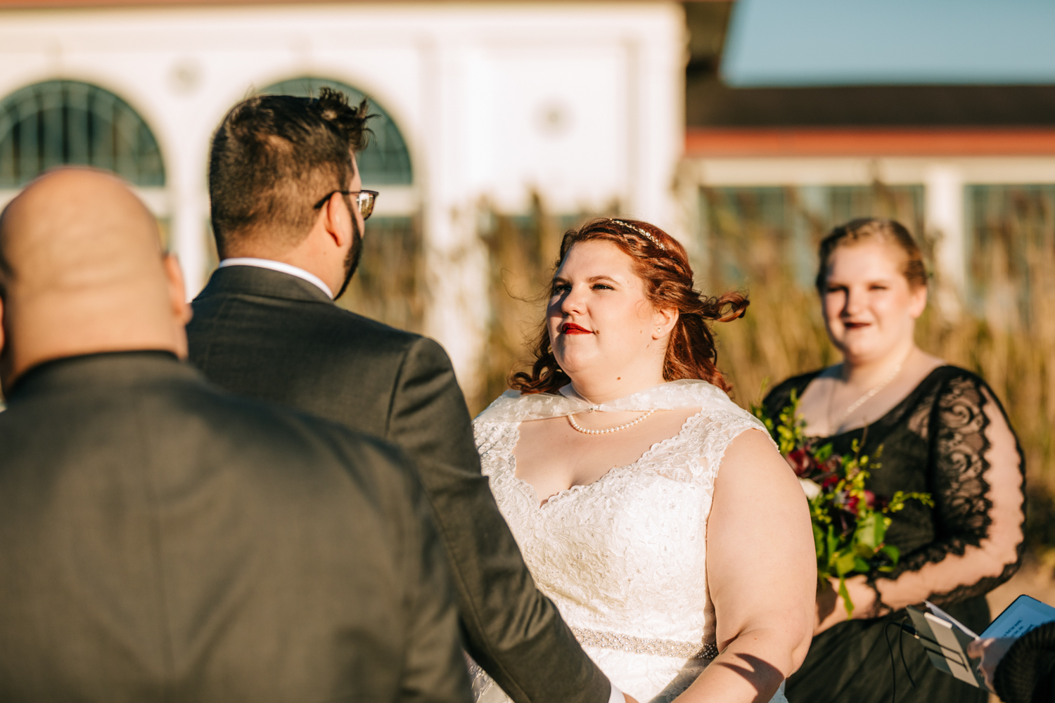 Bride wearing wedding cape looking at groom on beach wedding