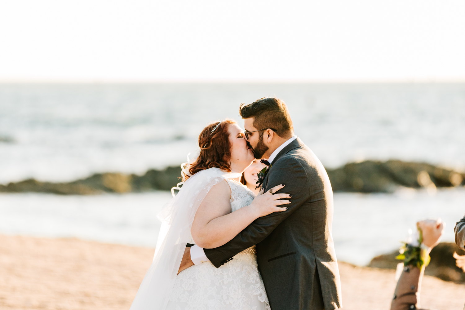 cape wearing bride and groom first kiss on beach wedding ceremony