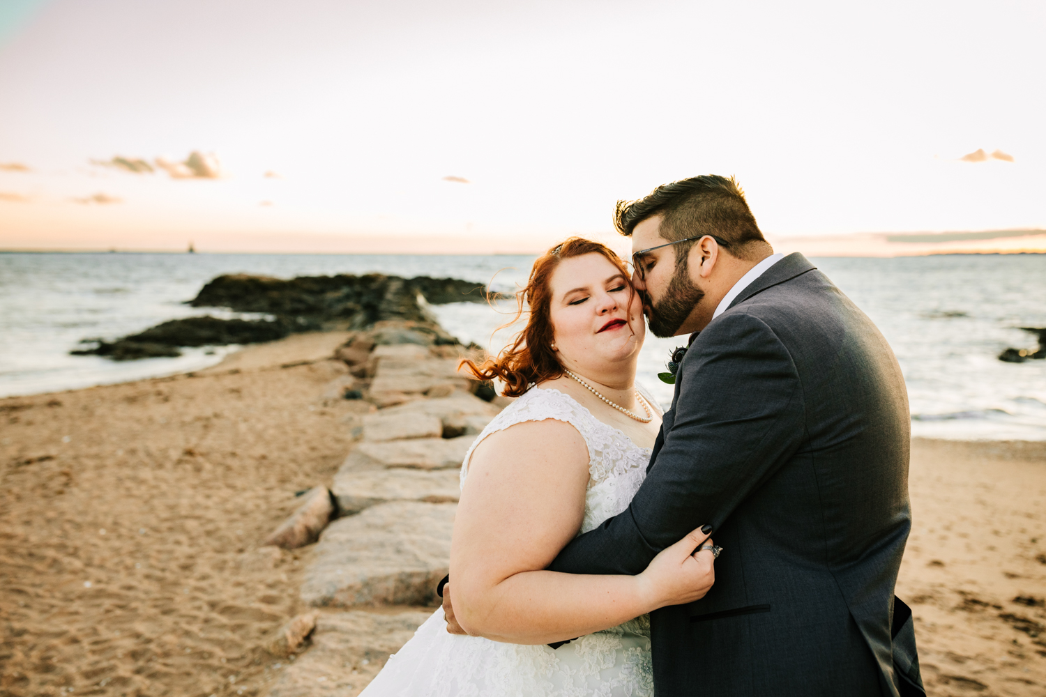 Groom kissing bride on rocks at ocean wedding