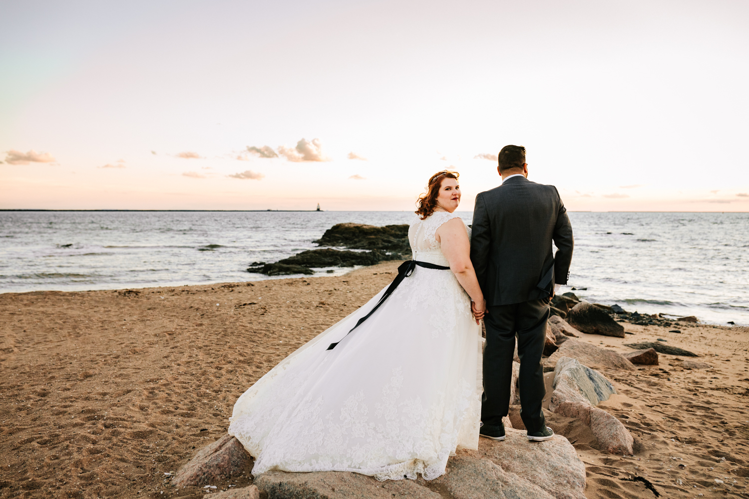 Bride wearing black belt holding hands with groom at sea themed wedding