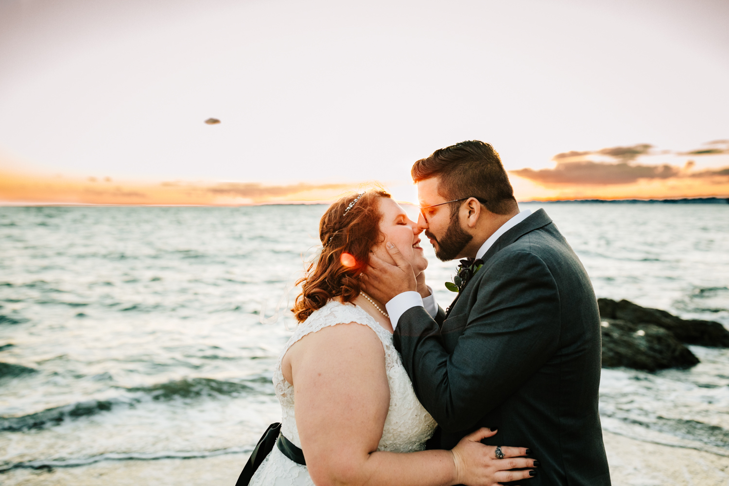 Bride and groom kissing with ocean at sunset