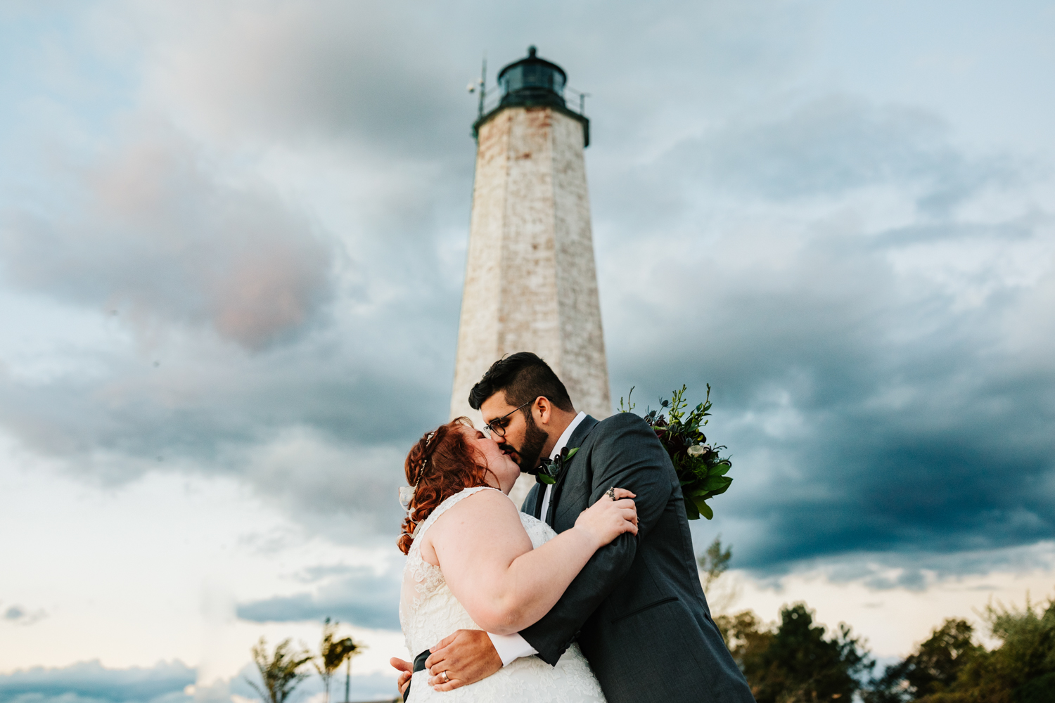 Bride and groom kissing under lighthouse on beach wedding