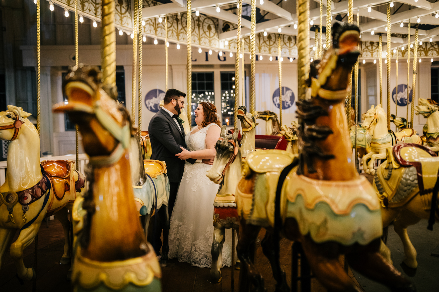 Bride and groom on carousel on wedding day surrounded by merry-go-round horses