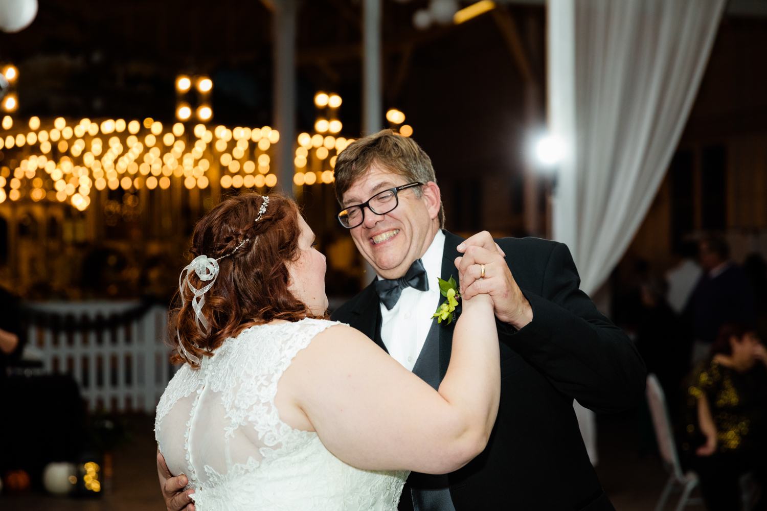 Bride and dad dance in front of carousel lights