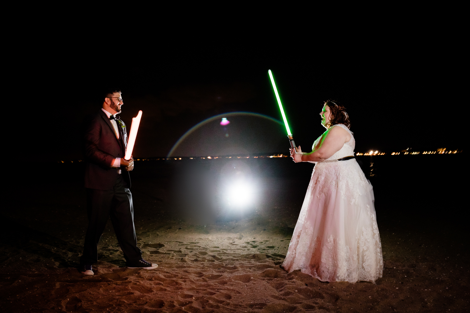 Bride and groom fighting with lightsabers on beach on wedding day