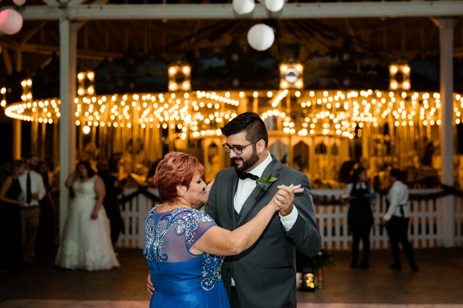 Groom dancing in front of mom in front of carousel