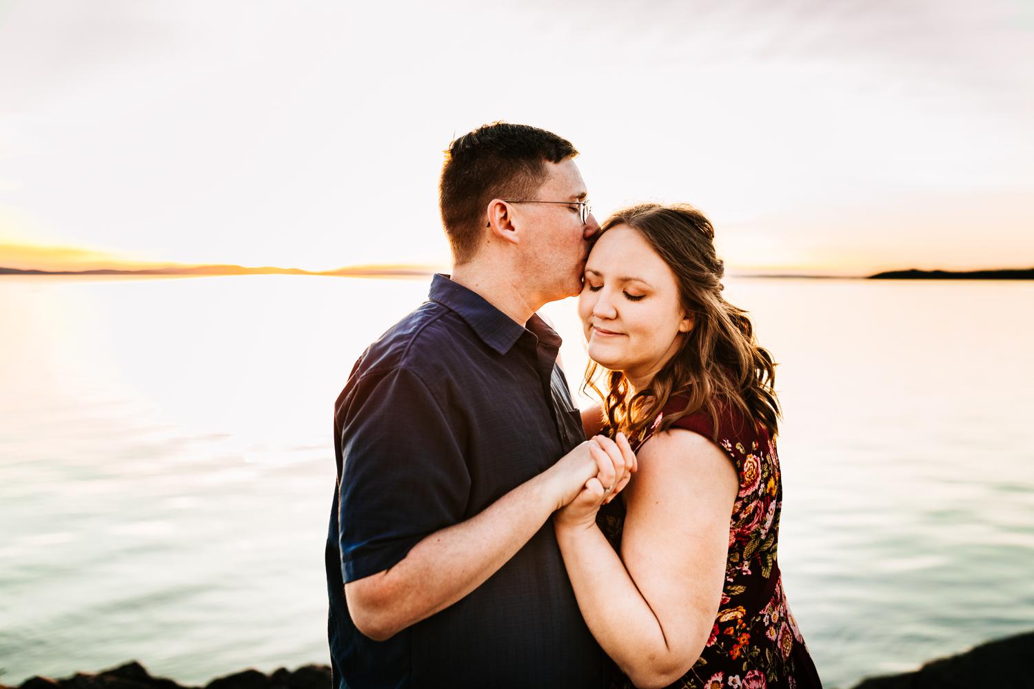 Man kissing girl at engagement session during sunset in front of mountains