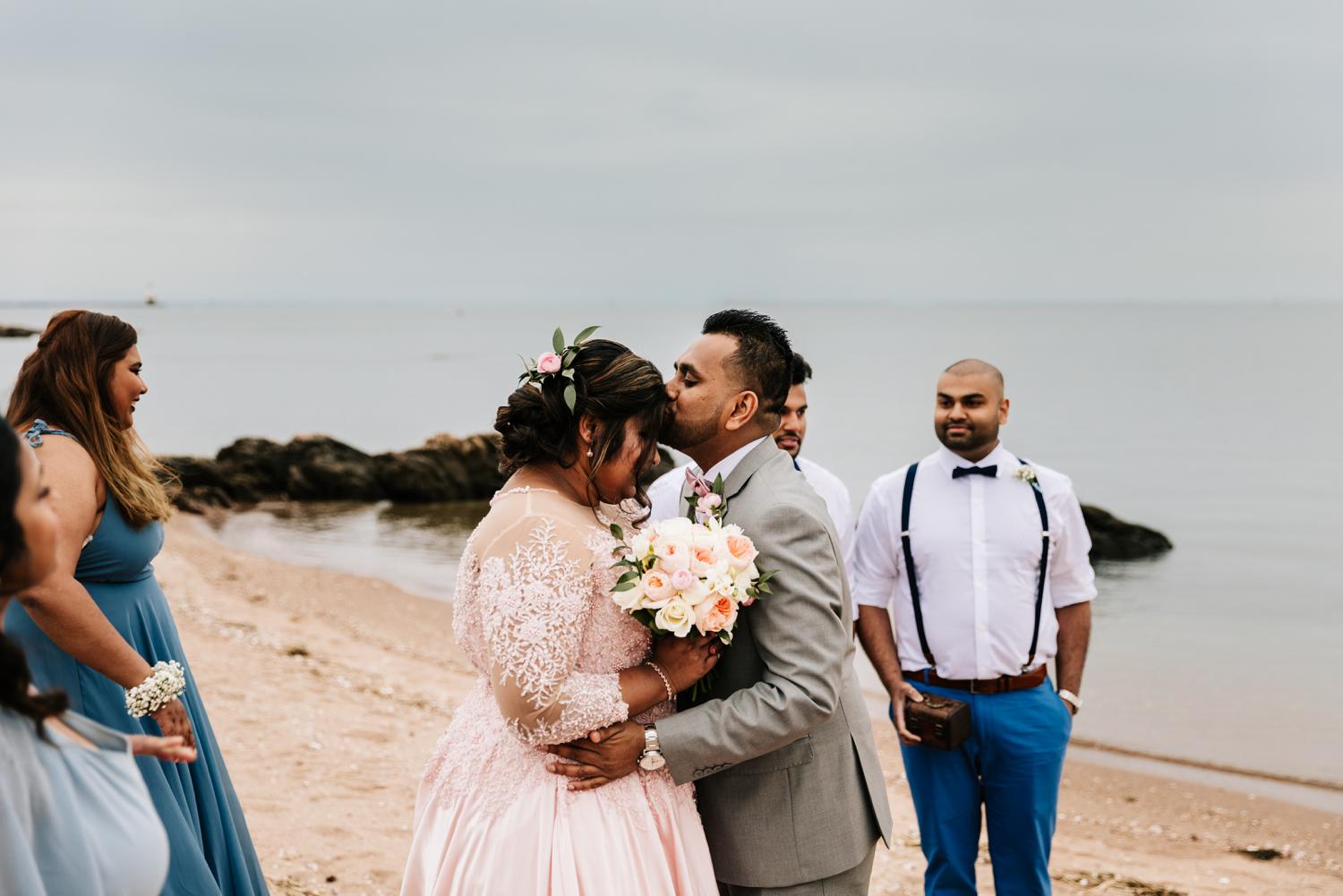 Groom kissing bride's forehead during intimate beach wedding