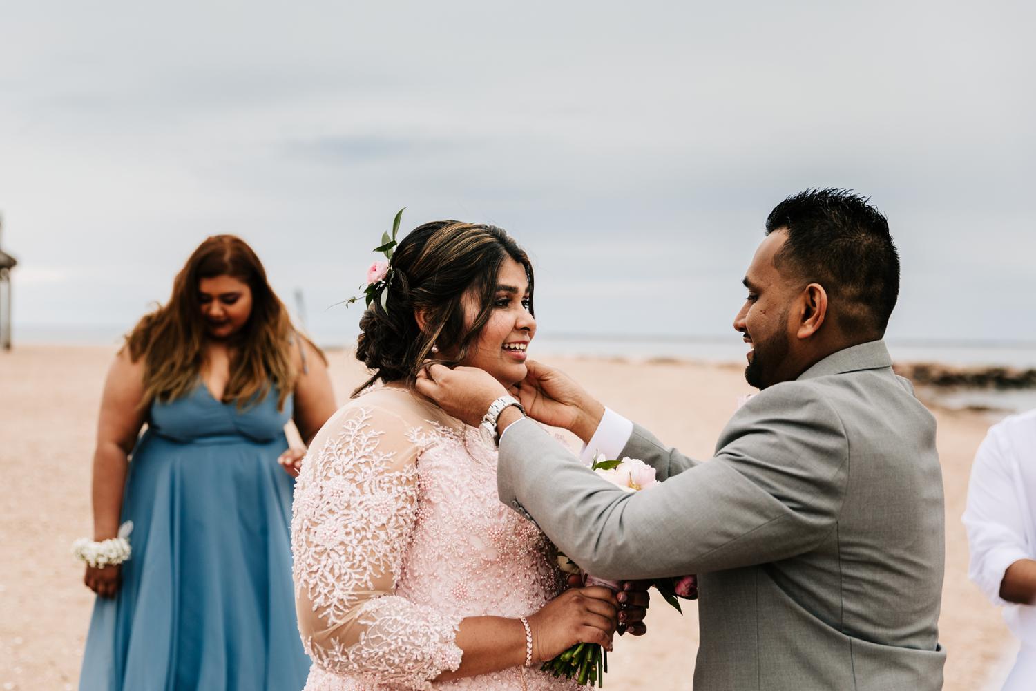 Groom putting necklace on bride wearing pink wedding dress