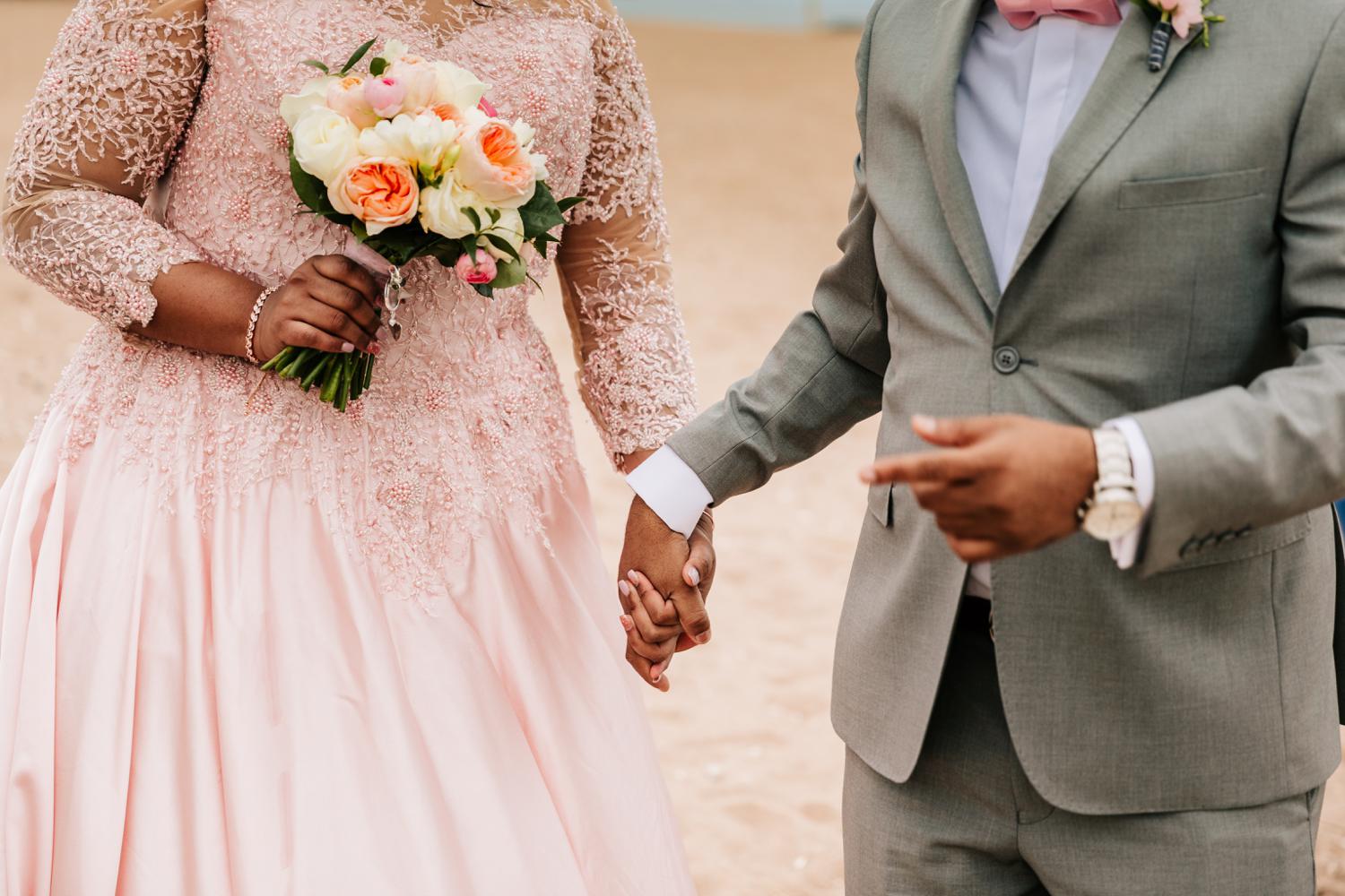 Bride and groom holding hands while bride holds rose bouquet