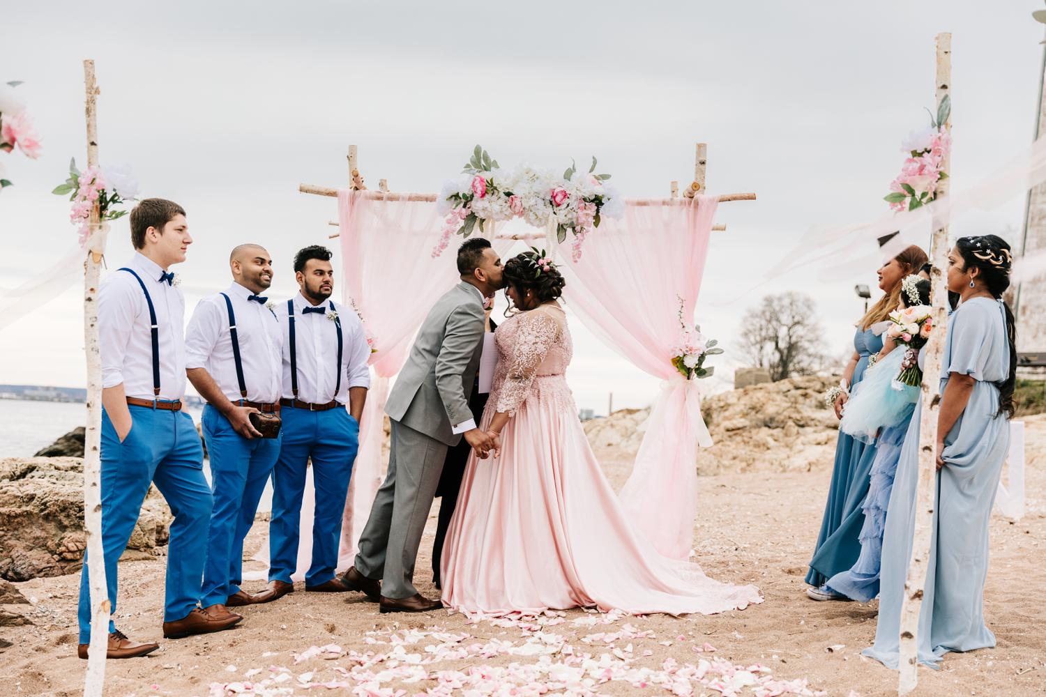 Groom kissing bride's forehead during wedding ceremony on beach