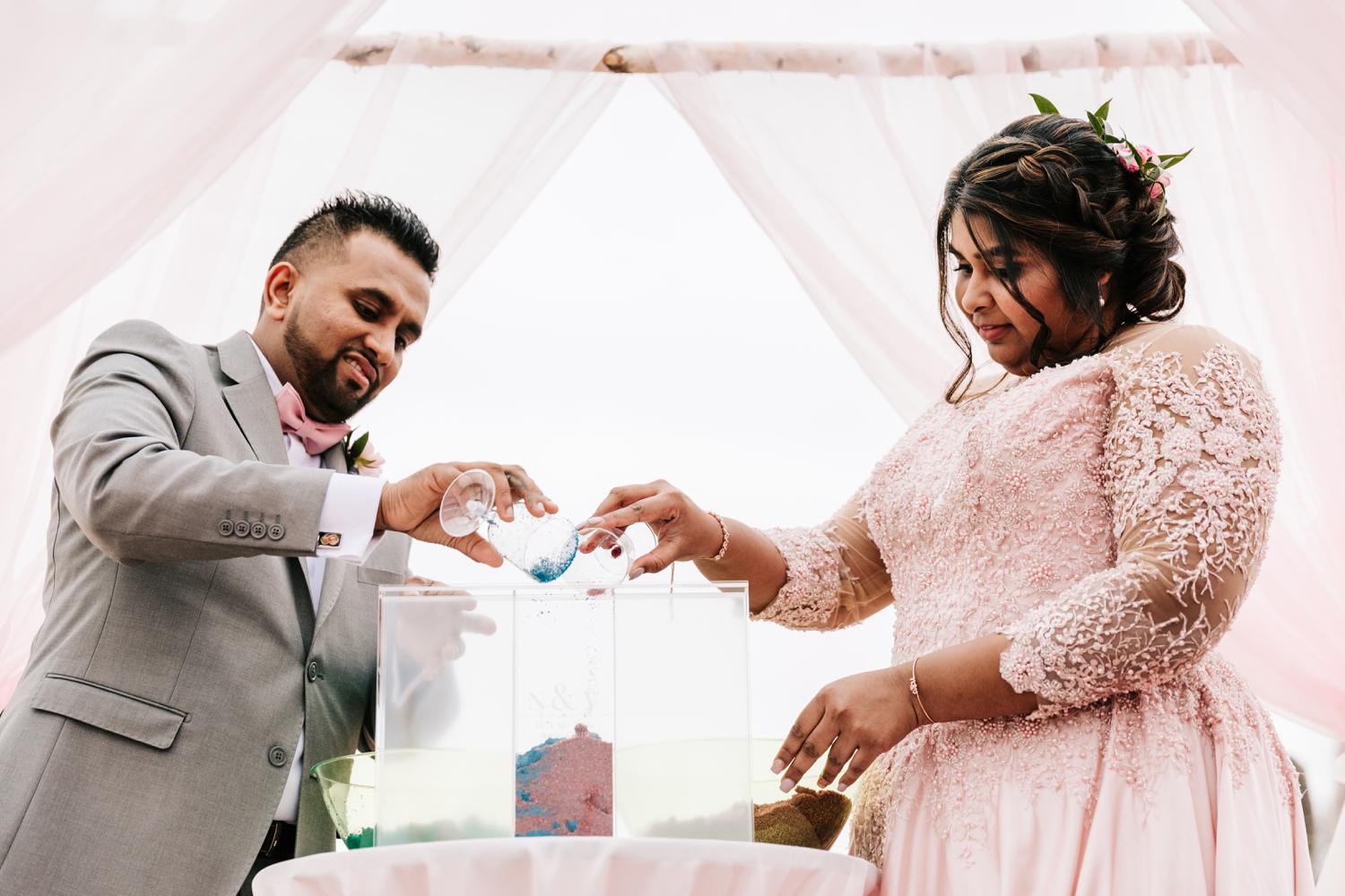 Sand ceremony at beach wedding with bride wearing pink dress