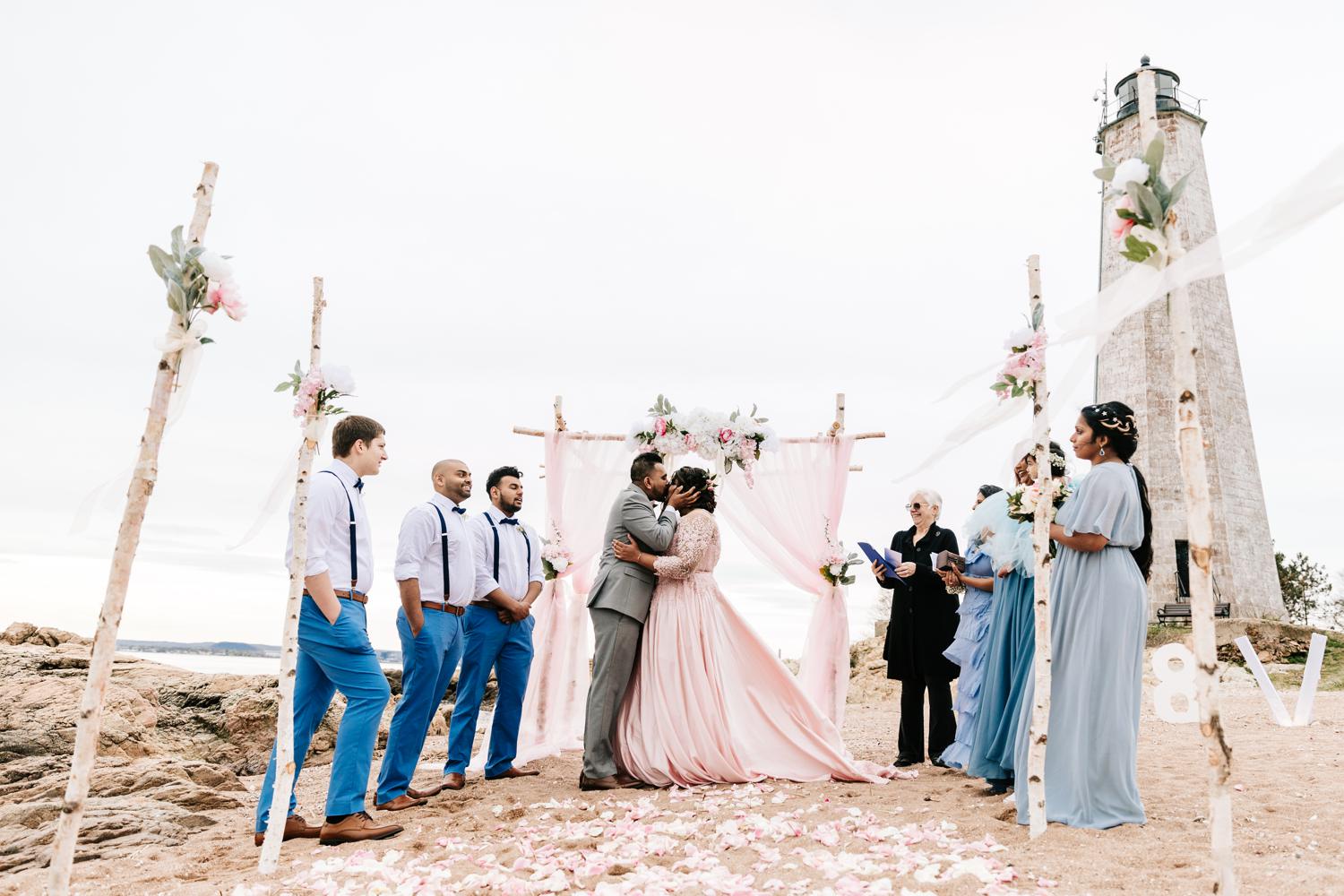 Bride and groom's first kiss on intimate beach wedding ceremony with birch tree and rose decorations