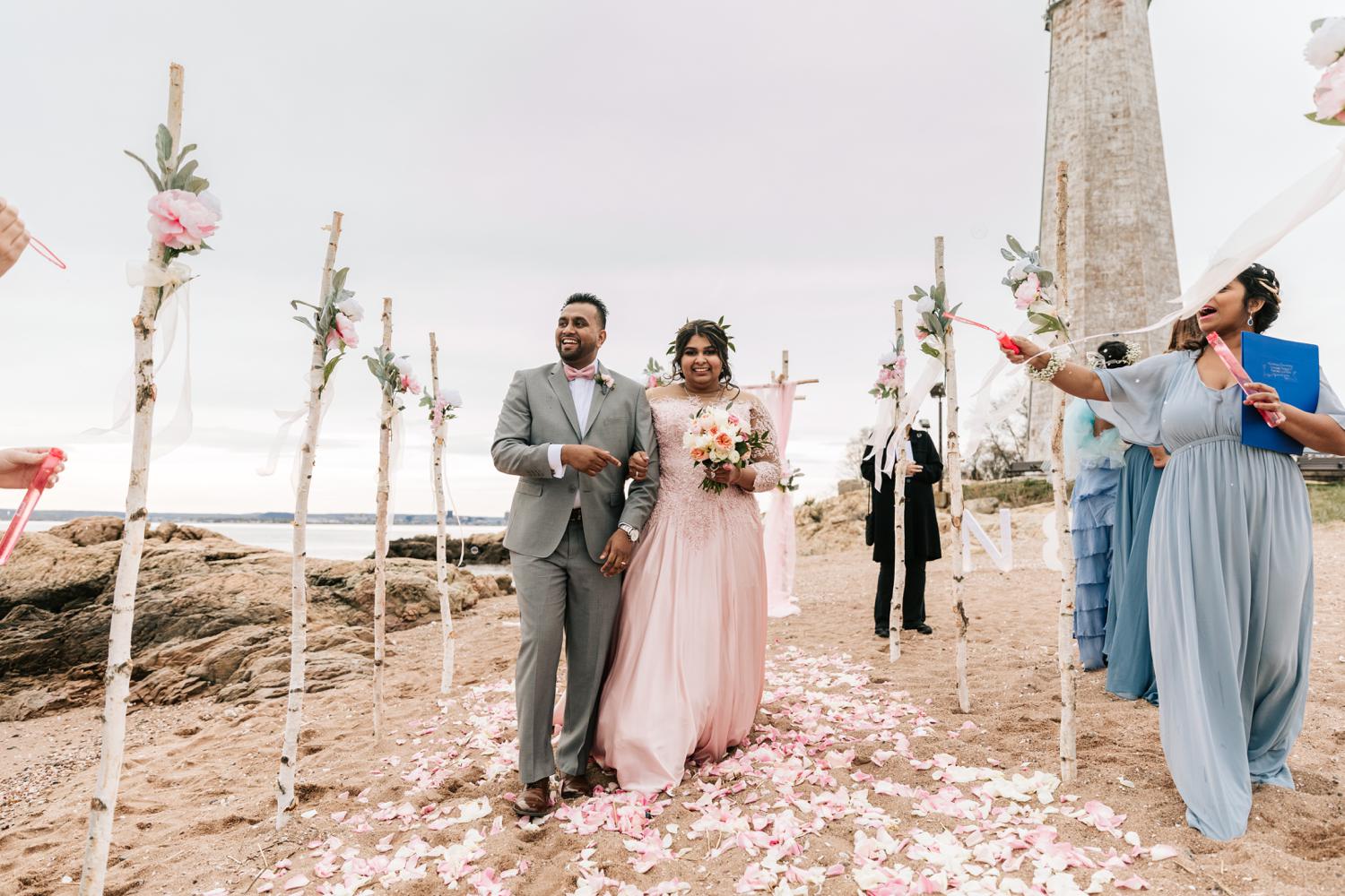 Bride and groom smiling walking down aisle of birch trees with bubbles