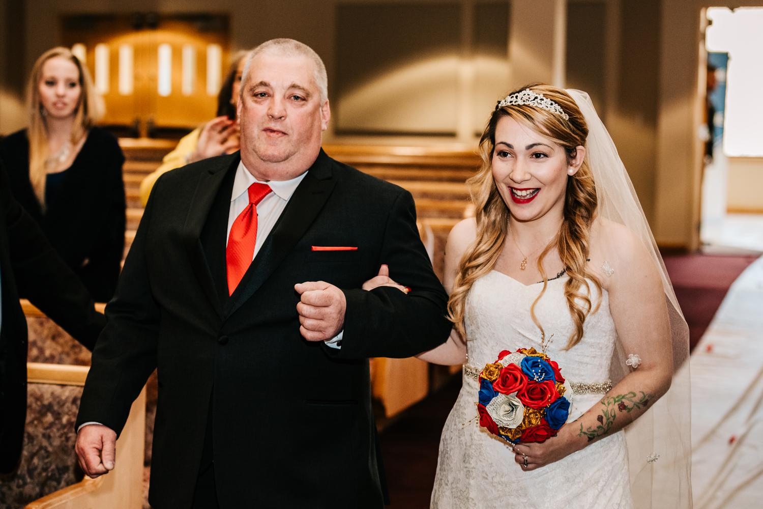 smiling bride in tiara being walked down aisle by father