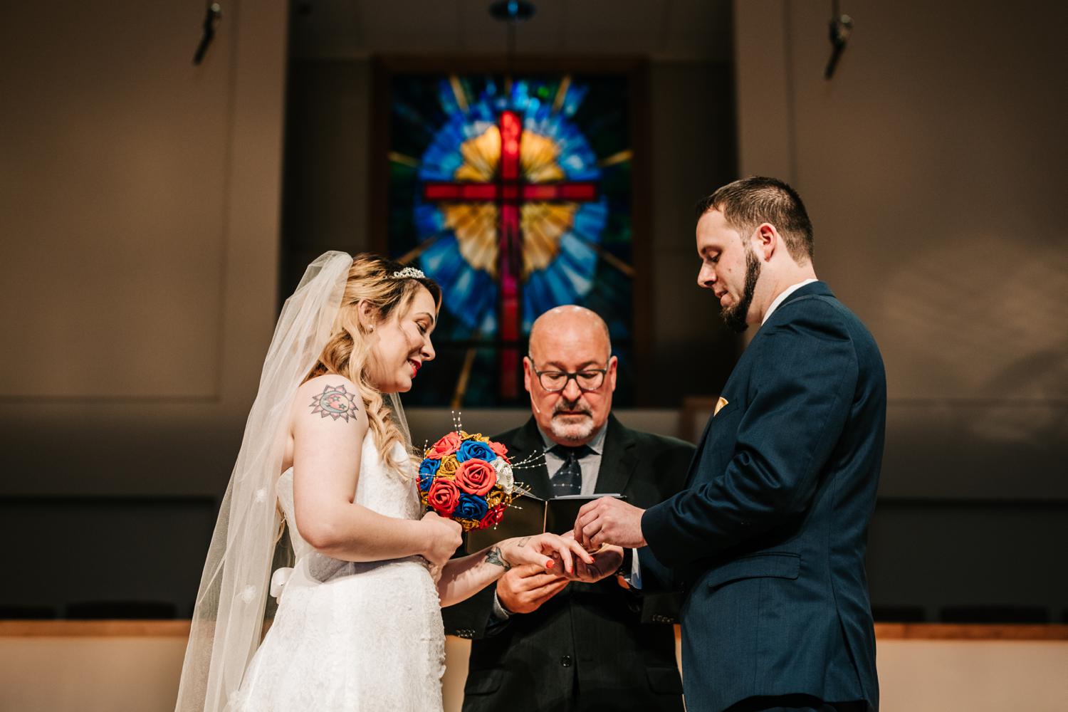 Groom giving tattooed bride ring during wedding ceremony