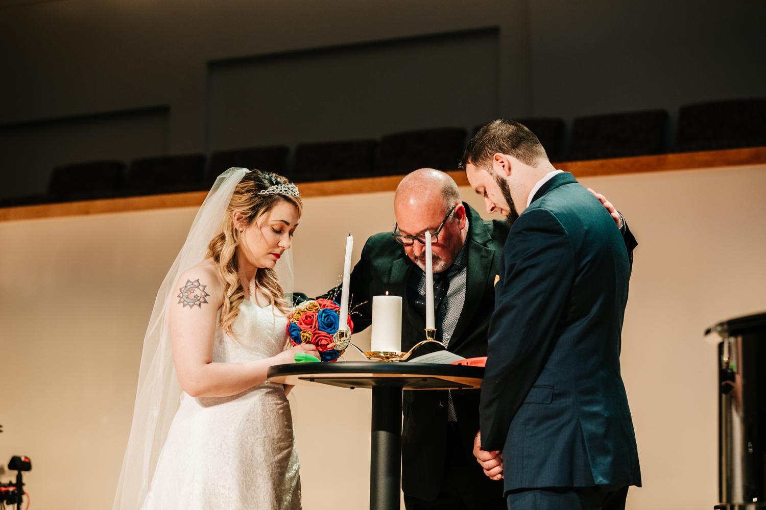 Tattooed bride and groom praying at wedding