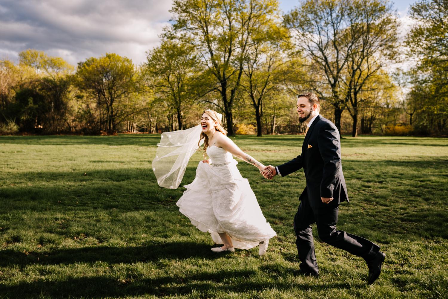 Tattoed bride and groom running through field in spring sunlight