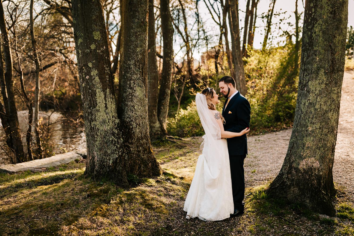 Bride and groom embracing in trees at park with tattoos