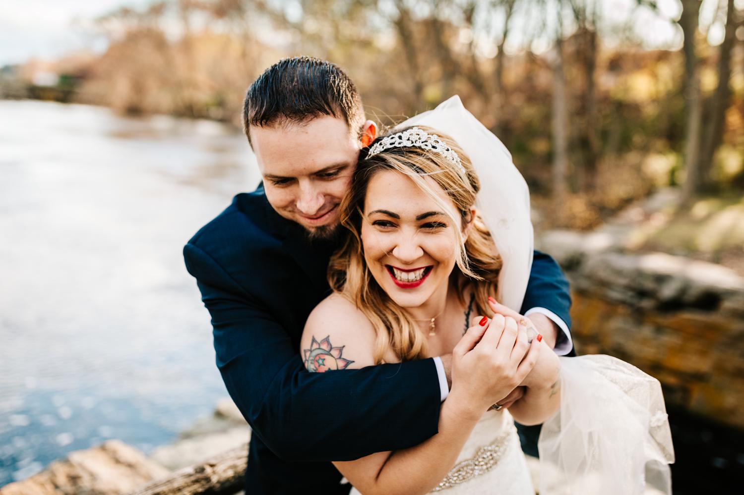 Laughing bride and groom wrapped up in eachother in front of water