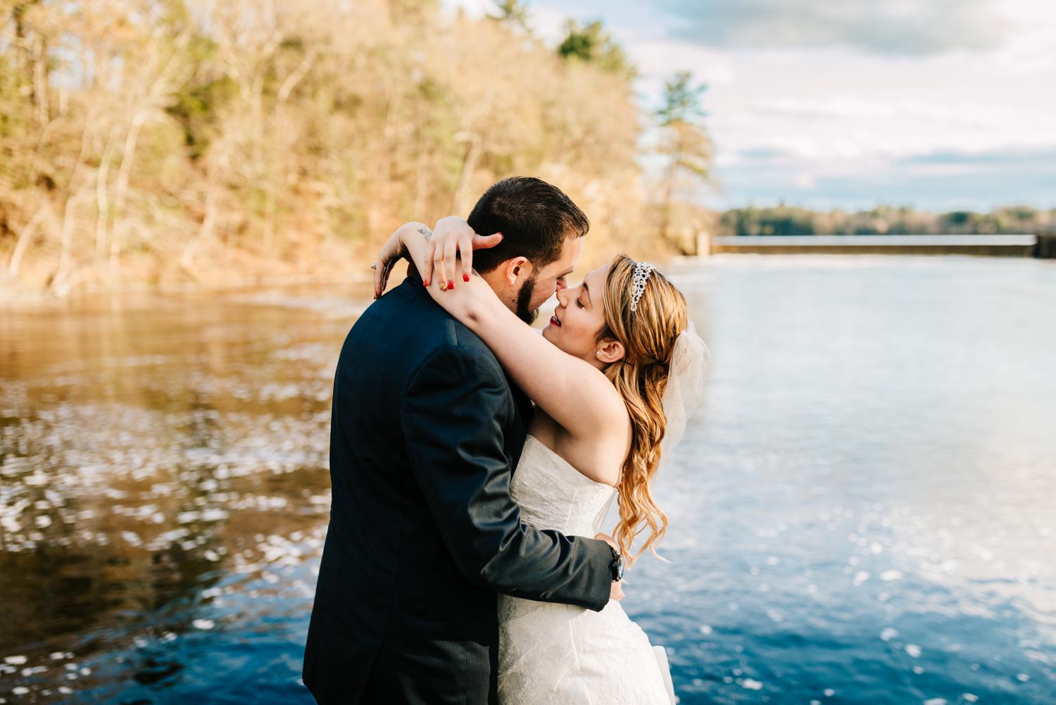 Tattooed bride and groom about to kiss at lake