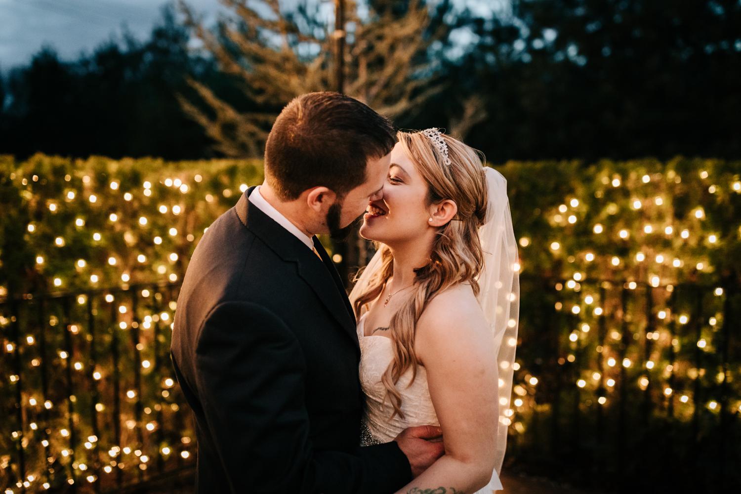 Bride and groom surrounded by lights at night kissing