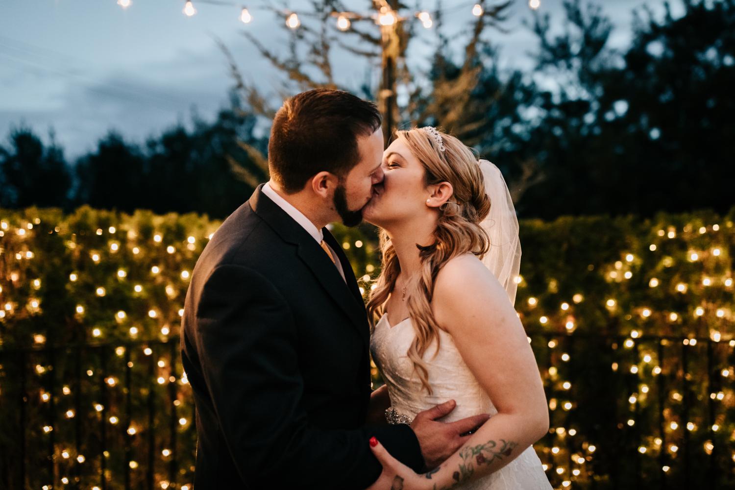 Tattooed bride and groom kissing with twinkle lights