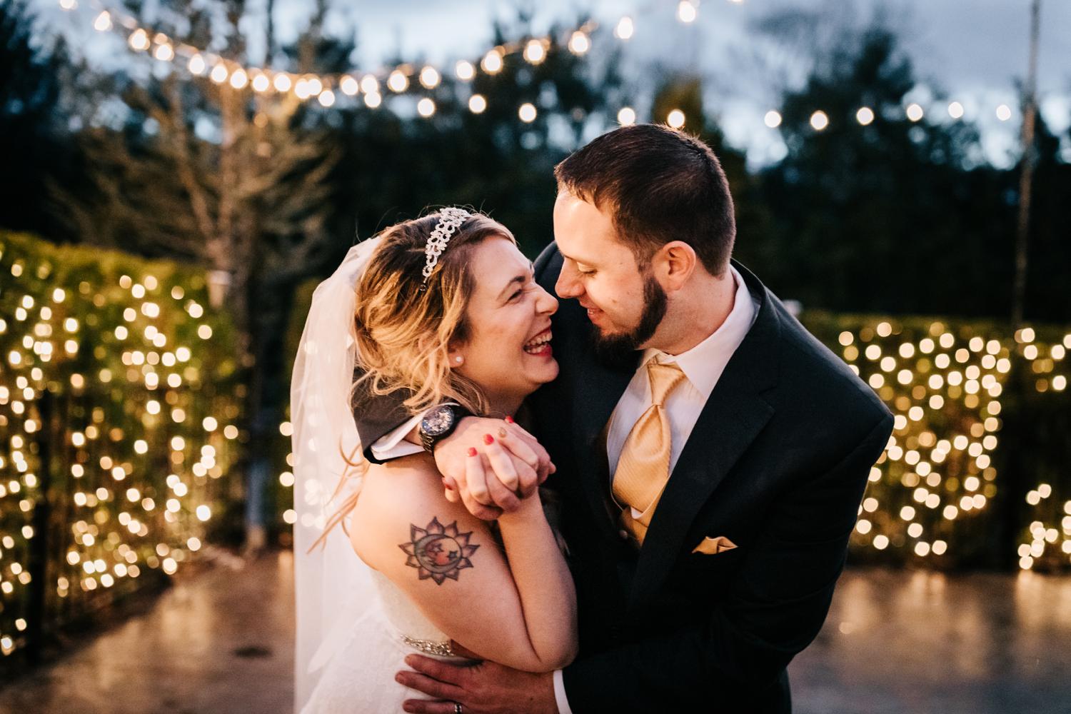 Bride and groom laughing and embracing under christmas lights at night