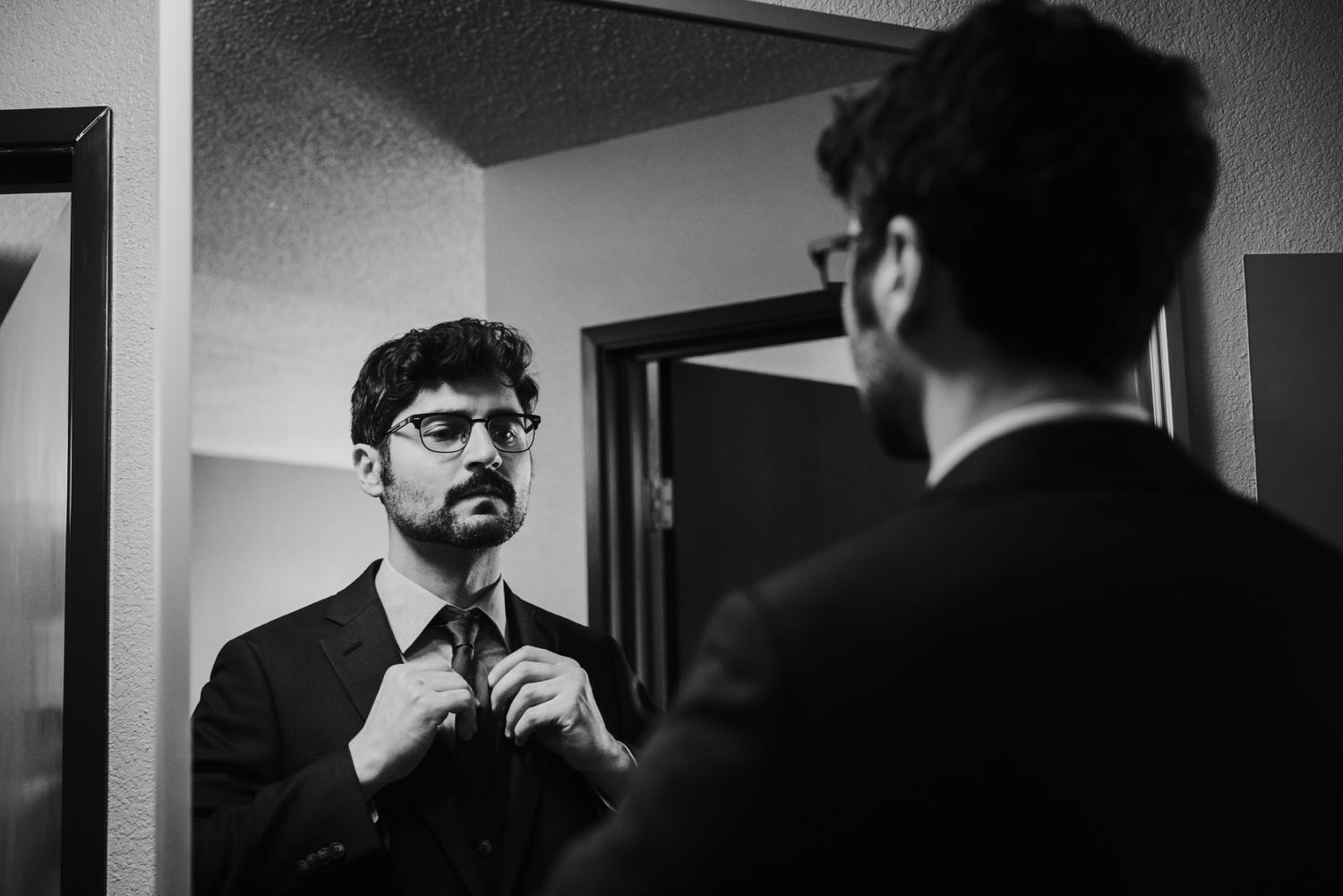 Groom putting on tie in mirror in Santa Fe hotel