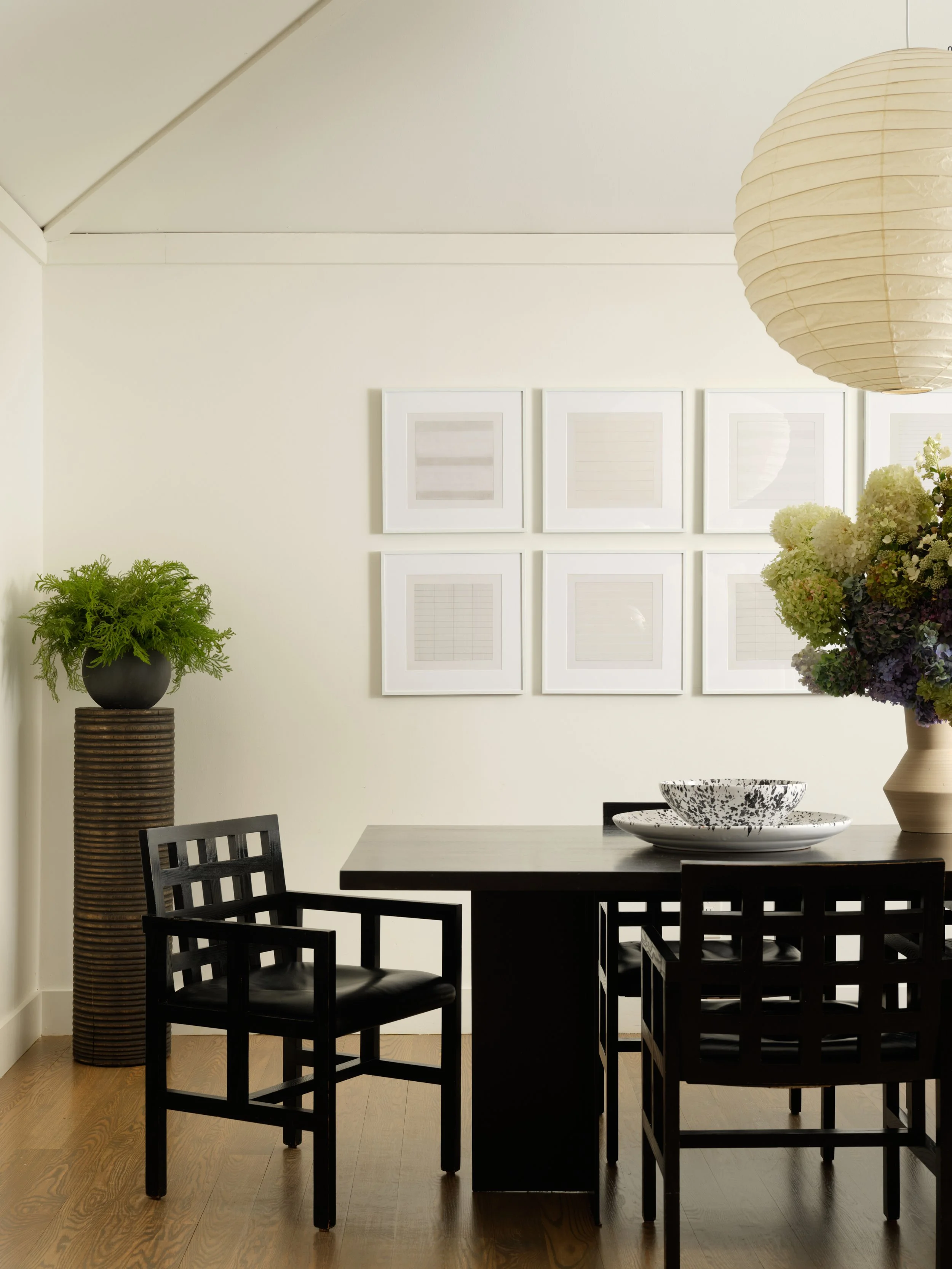Dining room corner in the Bedford project with black lattice-back chairs, a tall ribbed planter with a fern, and framed prints