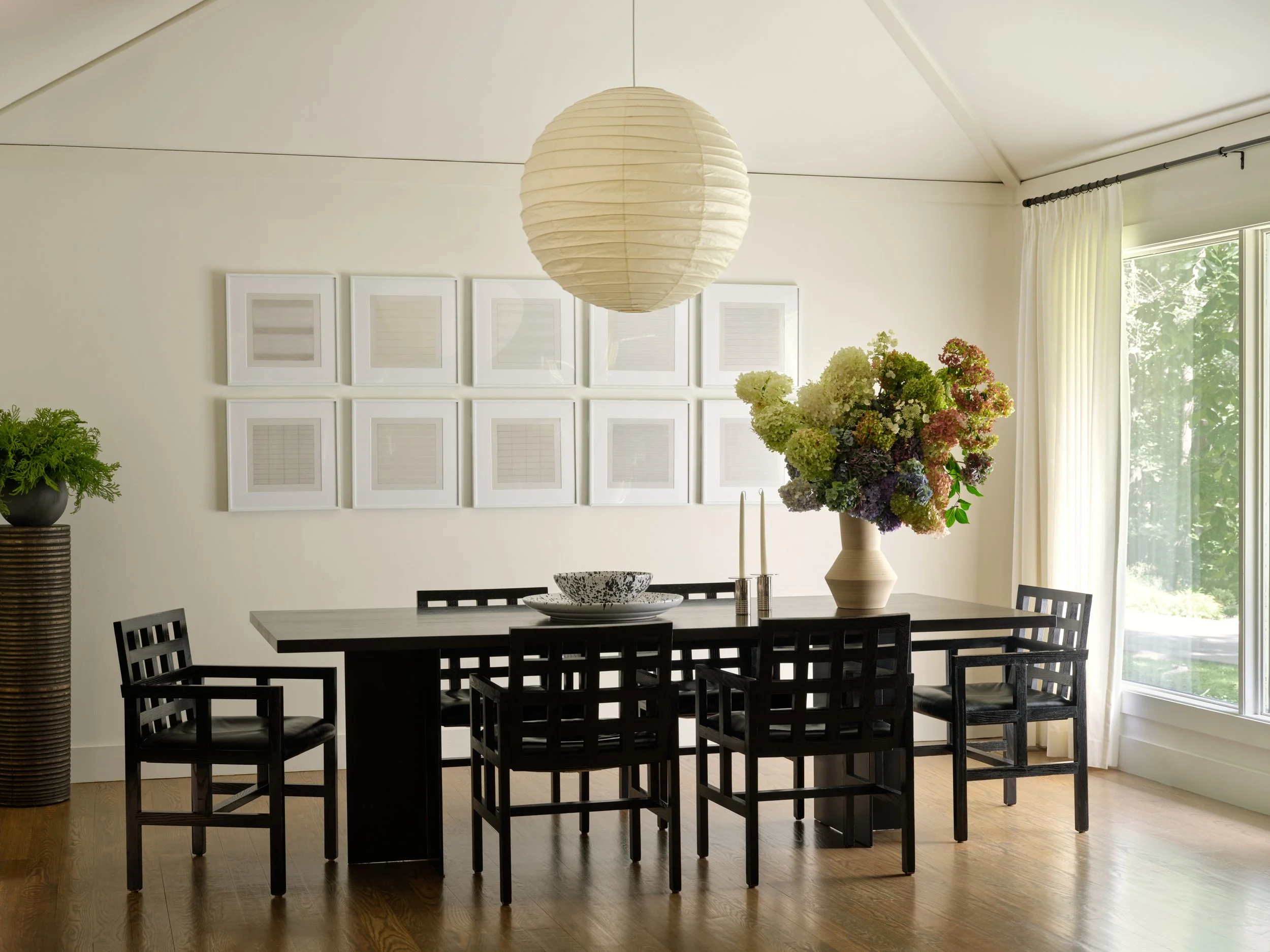 Dining room in the Bedford project with a black dining table, lattice-back chairs, a paper lantern pendant, and a grid of framed prints