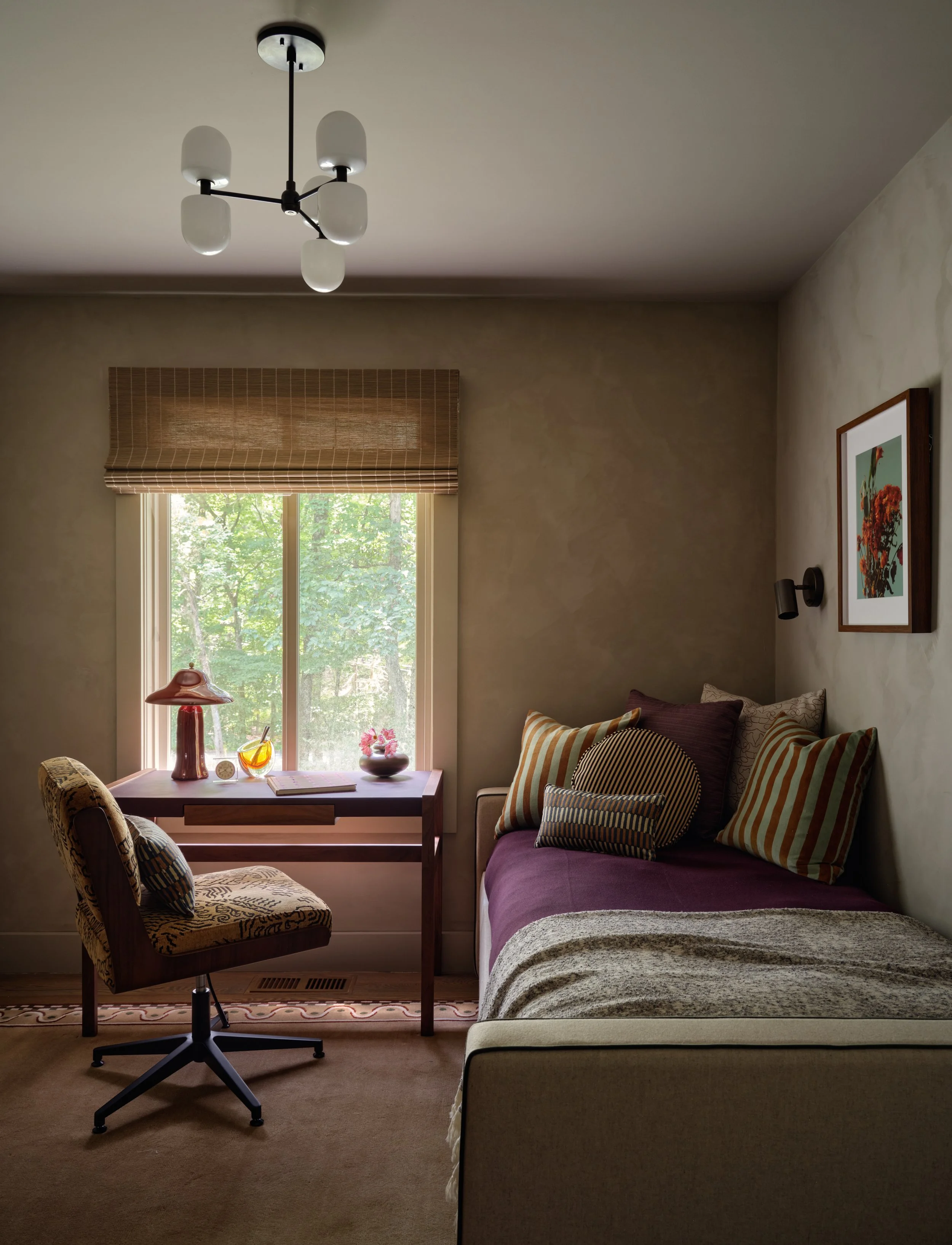 Bedroom in the Bedford project with a daybed, striped pillows, a wood desk with a patterned chair, and a woven roman shade