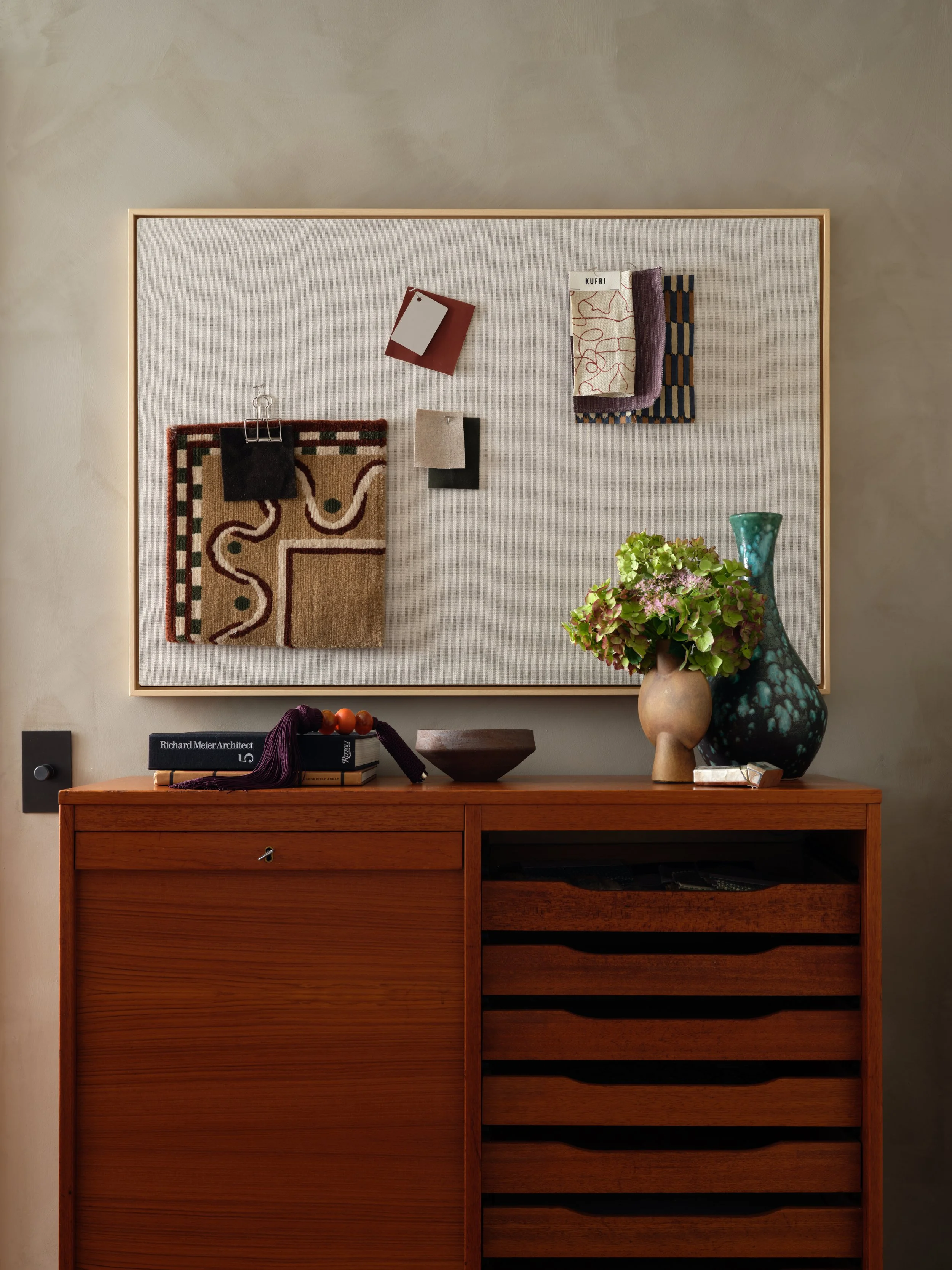 Wood dresser in the Bedford project with vases, art books, and a framed textile pinboard