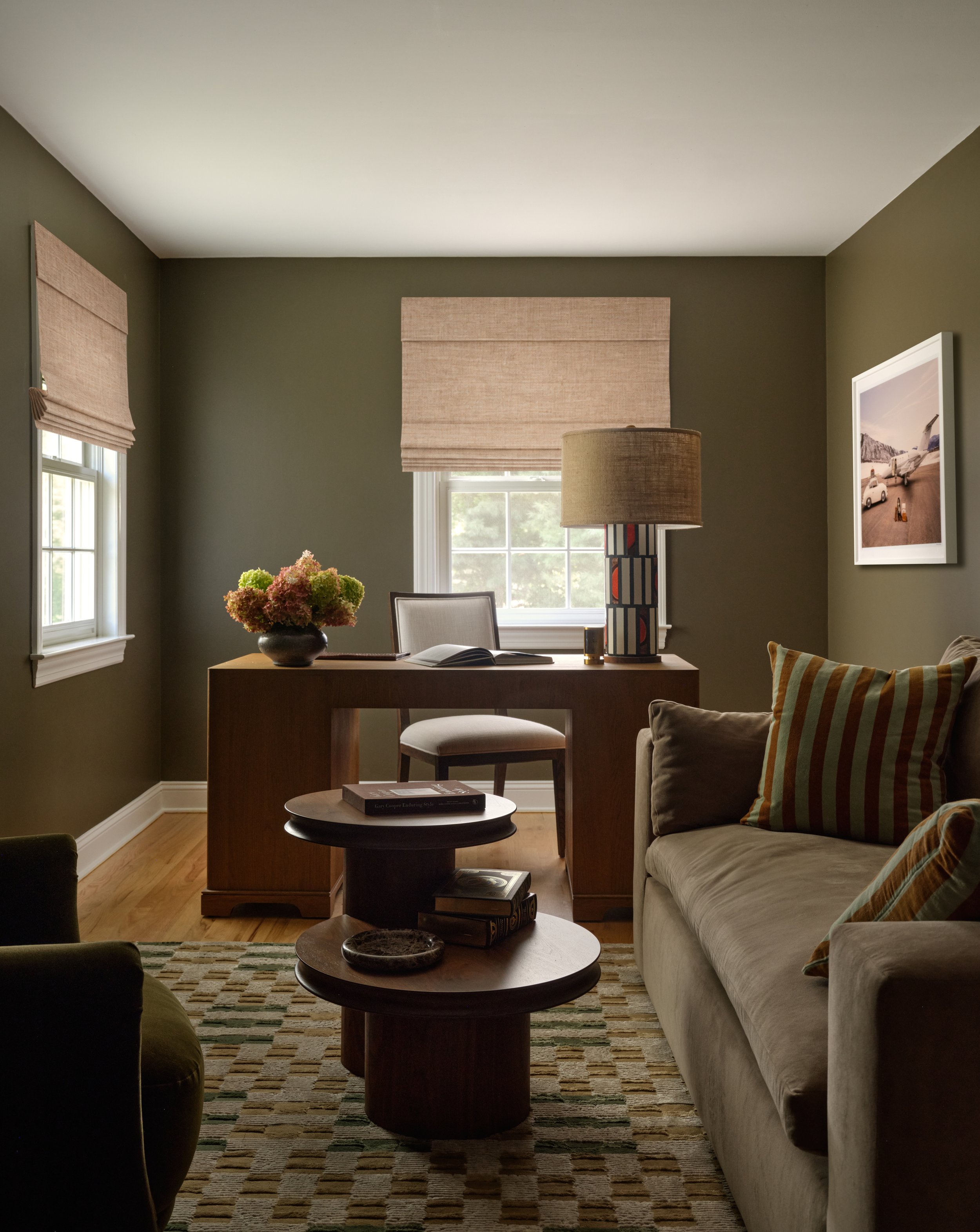 Study in the Bedford project with olive green walls, wood desk, and beige sofa with striped pillows
