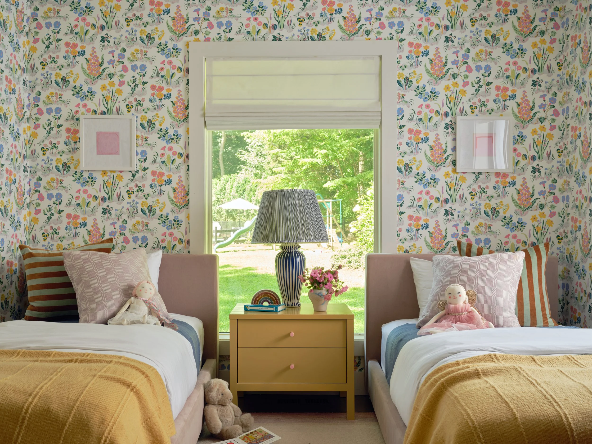 Girls room in the Bedford project with floral wallpaper, twin beds with mustard throws and striped pillows, and a shared yellow nightstand with a blue striped lamp