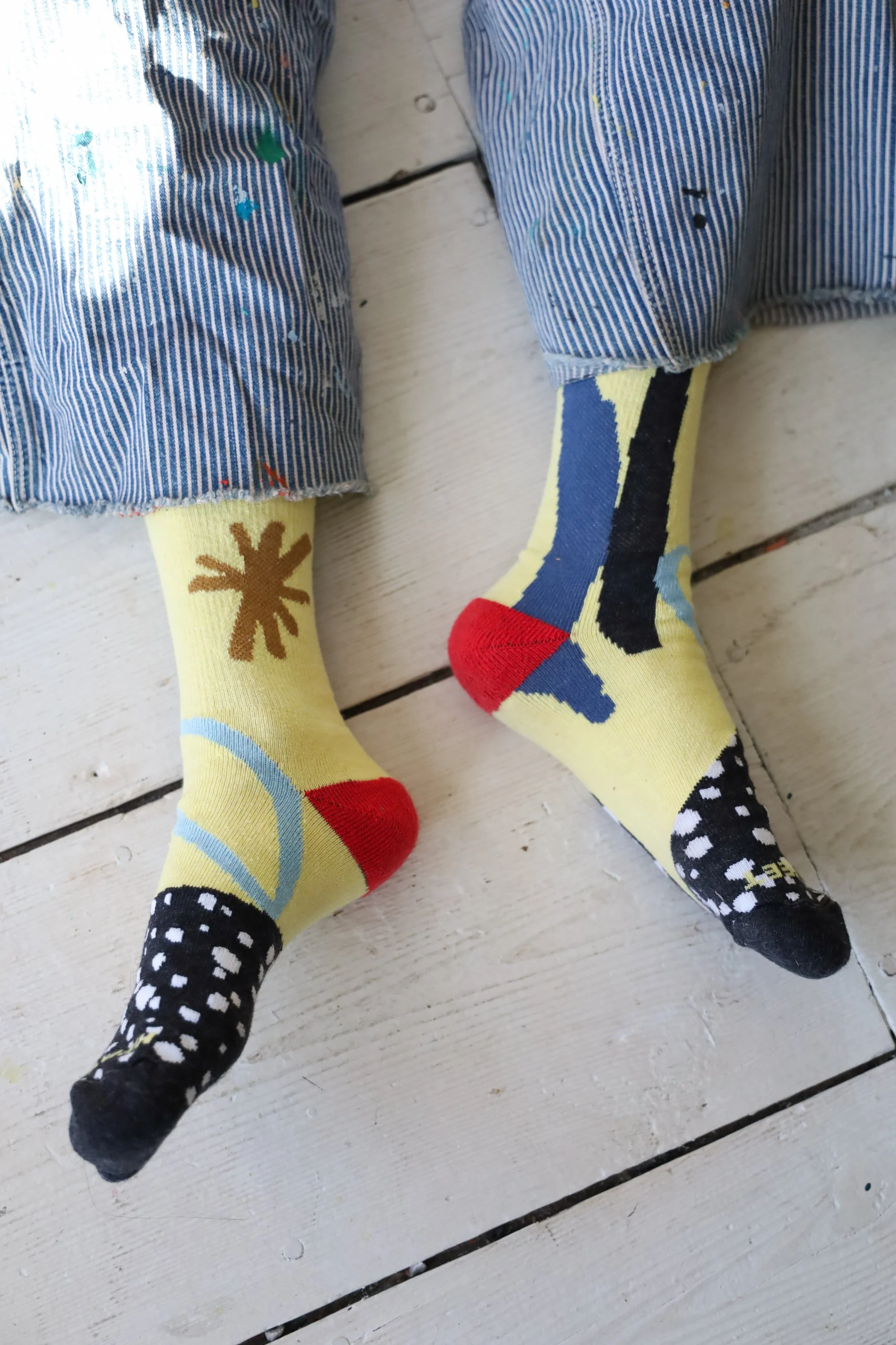 Pair of Hippy Feet "Doodle Socks" by artist Ashley Mary, featuring a light yellow base with playful, hand-drawn abstract shapes and "wonky" marks in vibrant colors.