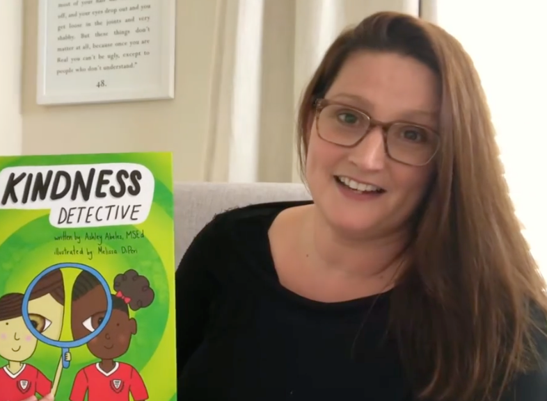 Author Ashley holding Kindness Detective book in her headshot