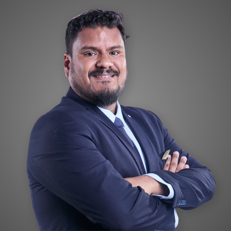 A man with a beard and short curly hair, smiling with arms crossed, wearing a checkered shirt in a modern, well-lit indoor setting.