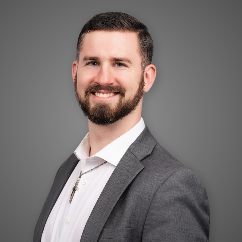 A man in a gray suit and white shirt smiling in a modern, well-lit indoor space.