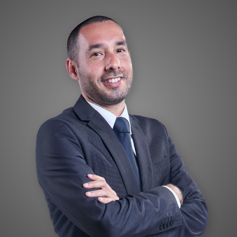 A smiling man in a green plaid button-up shirt standing in a spacious, well-lit corridor.