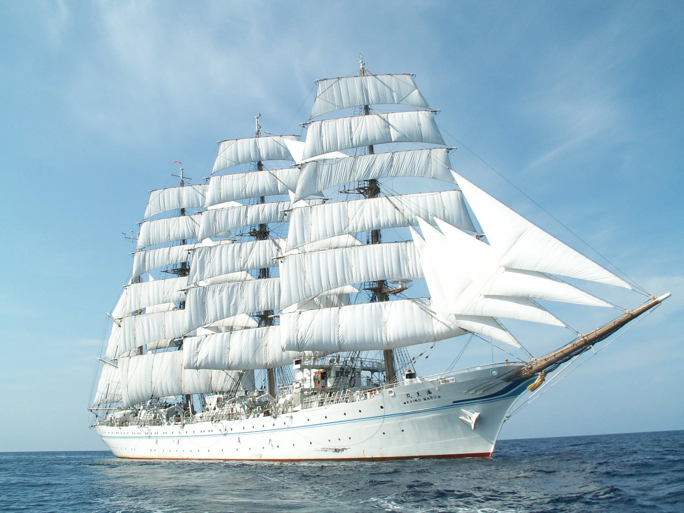 A large sailing ship with multiple white sails on a calm ocean under a clear blue sky.