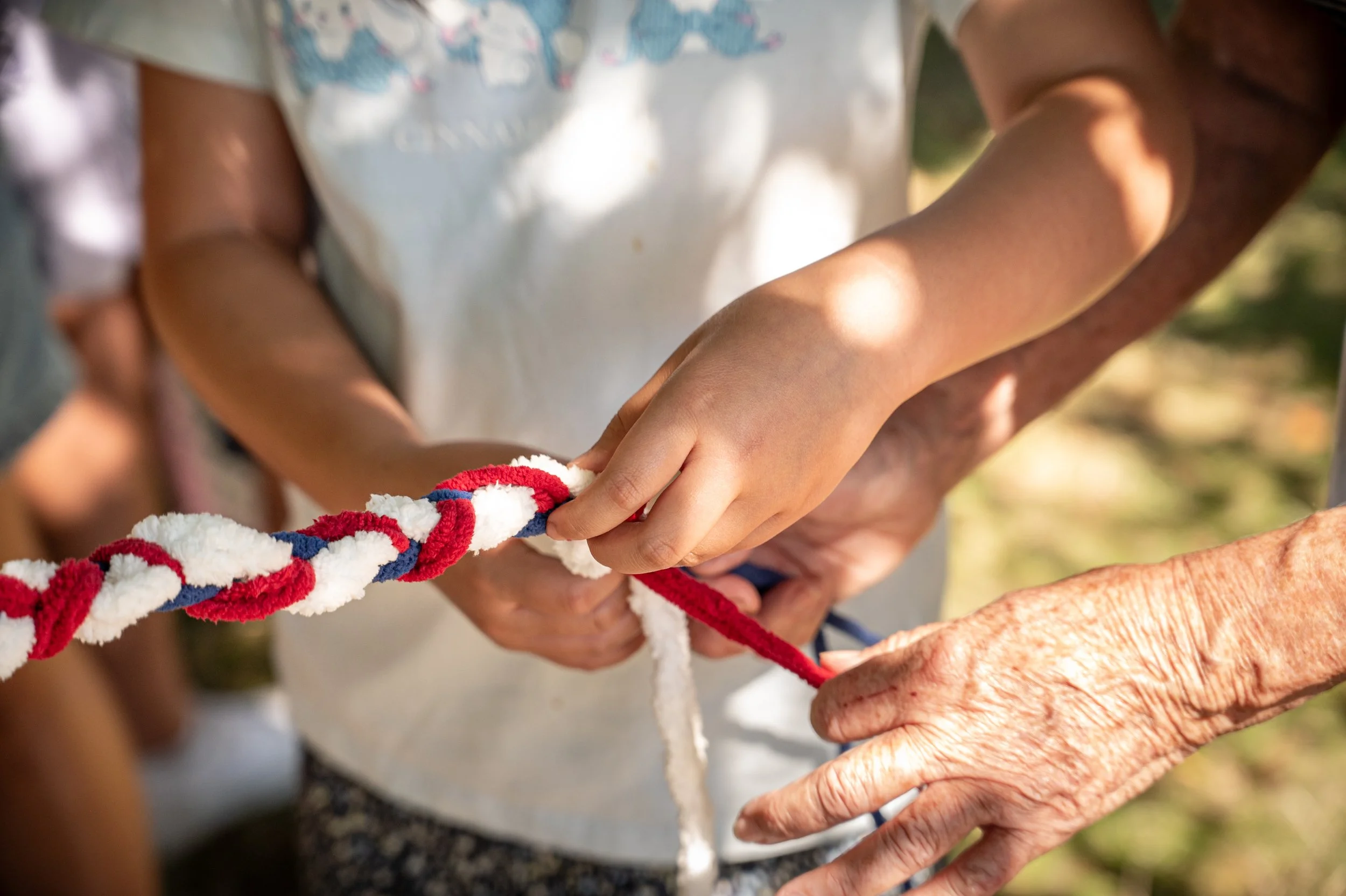 Close-up of two people tying a multicolored rope outdoors, with one person's hand appearing elderly and the other younger.
