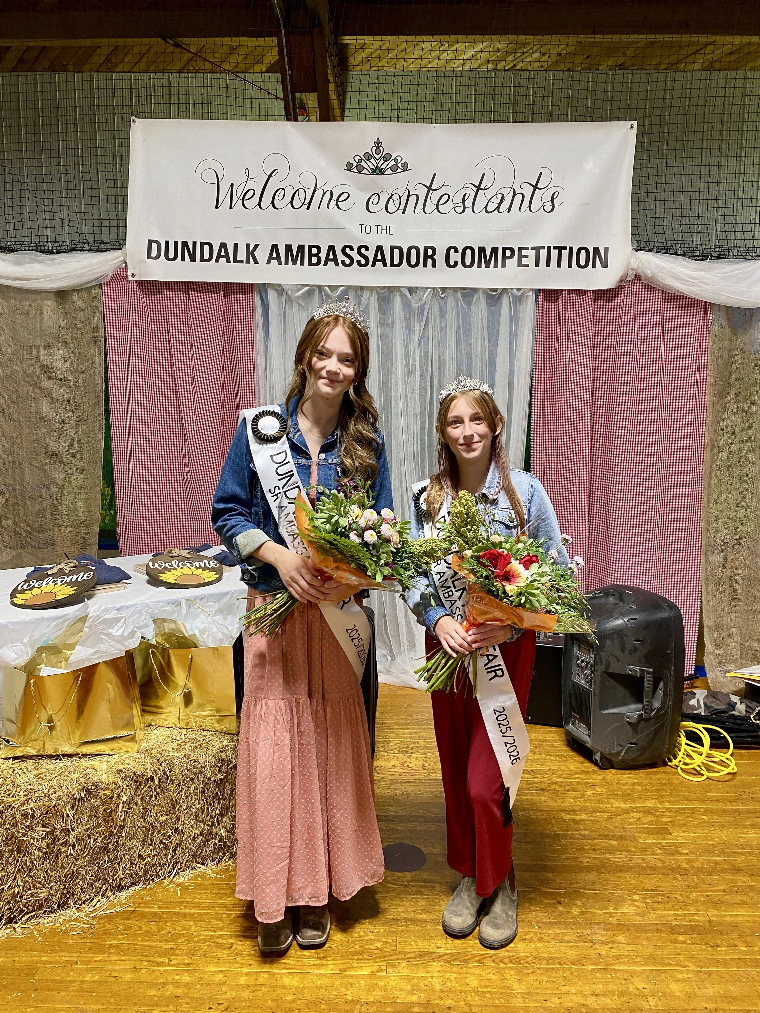 the 2025 Dundalk Fall Fair ambassadors standing beside each other on a wooden stage holding bouquets of flowers