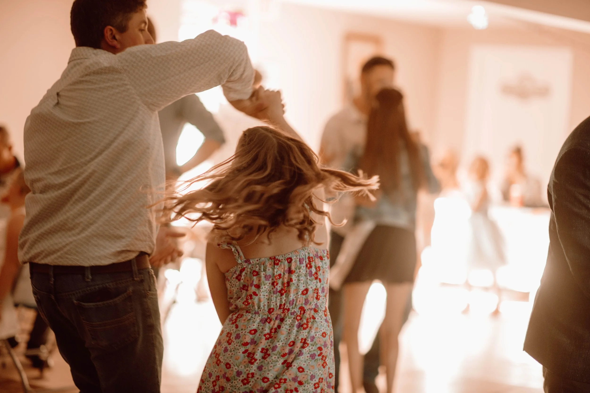 A dad and daughter dressed in formal attire are dancing. The dad is holding his daughter's hand while spinning her around.