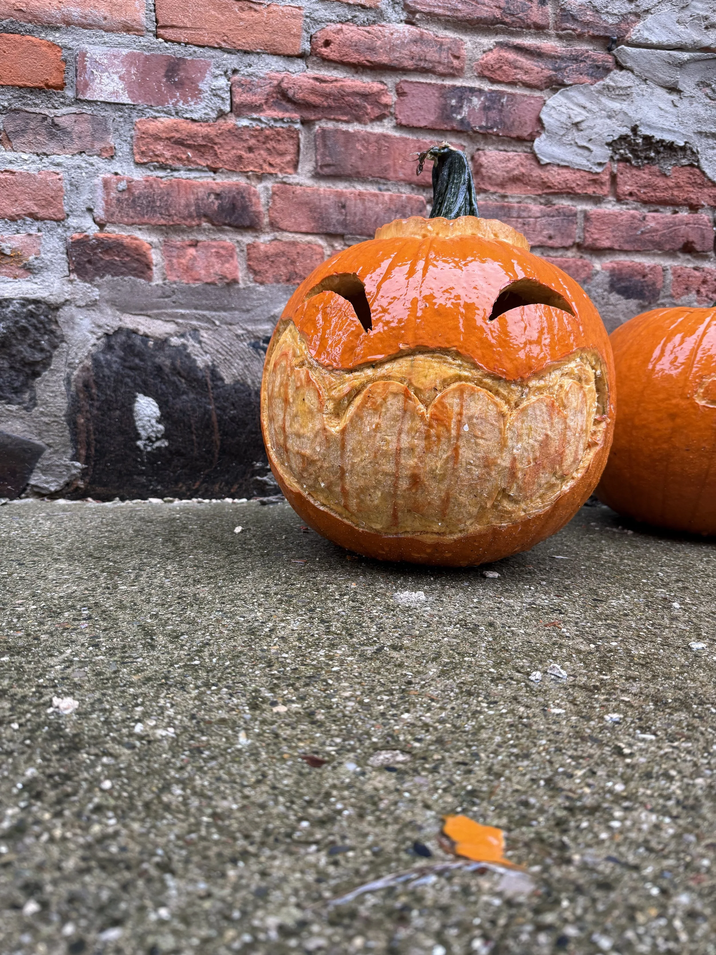 A carved jack o' lantern smiling in the rain on the ground against an old red brick building.