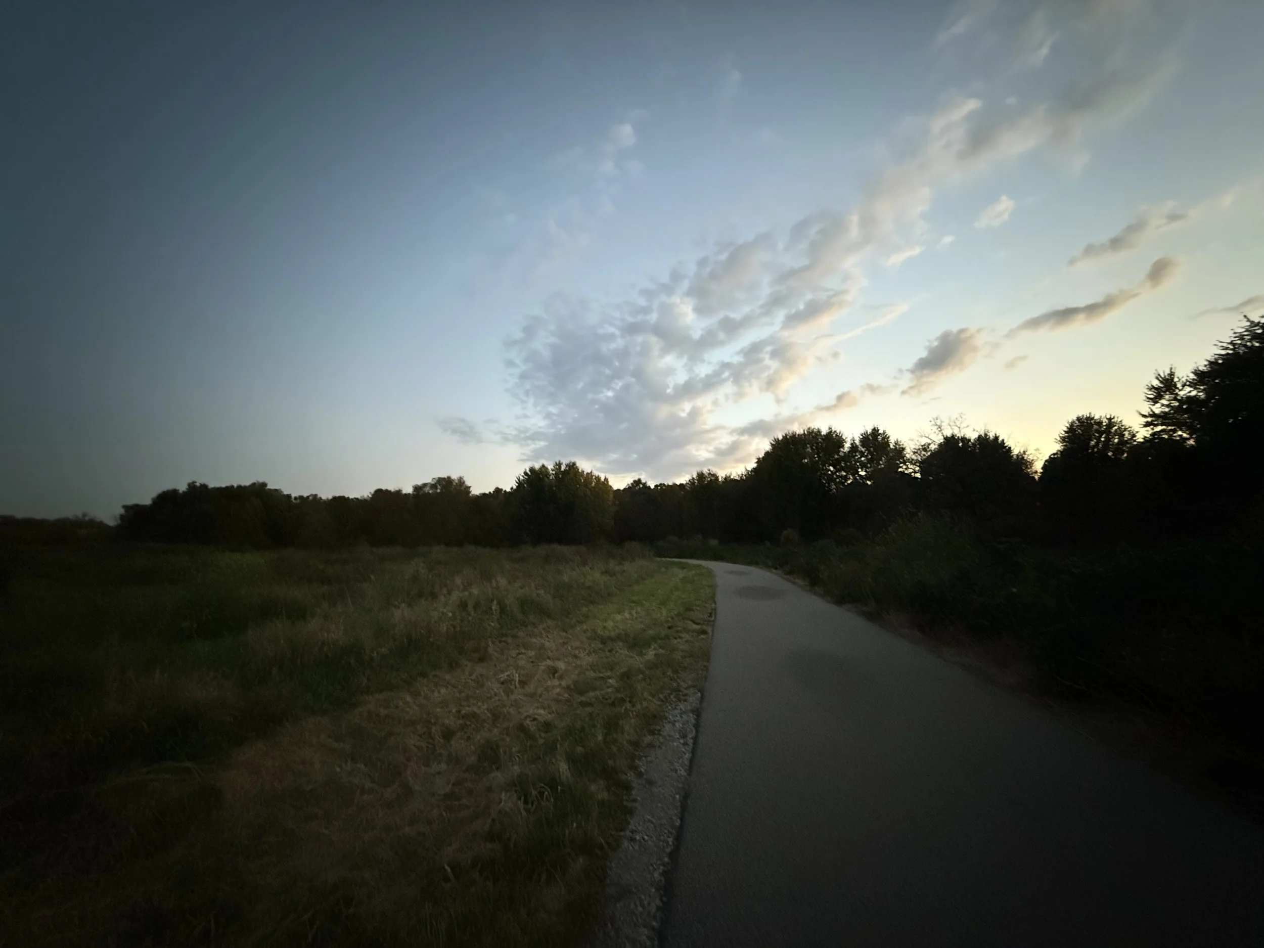 A path cuts between a creek and grasslands in October just after sunset.