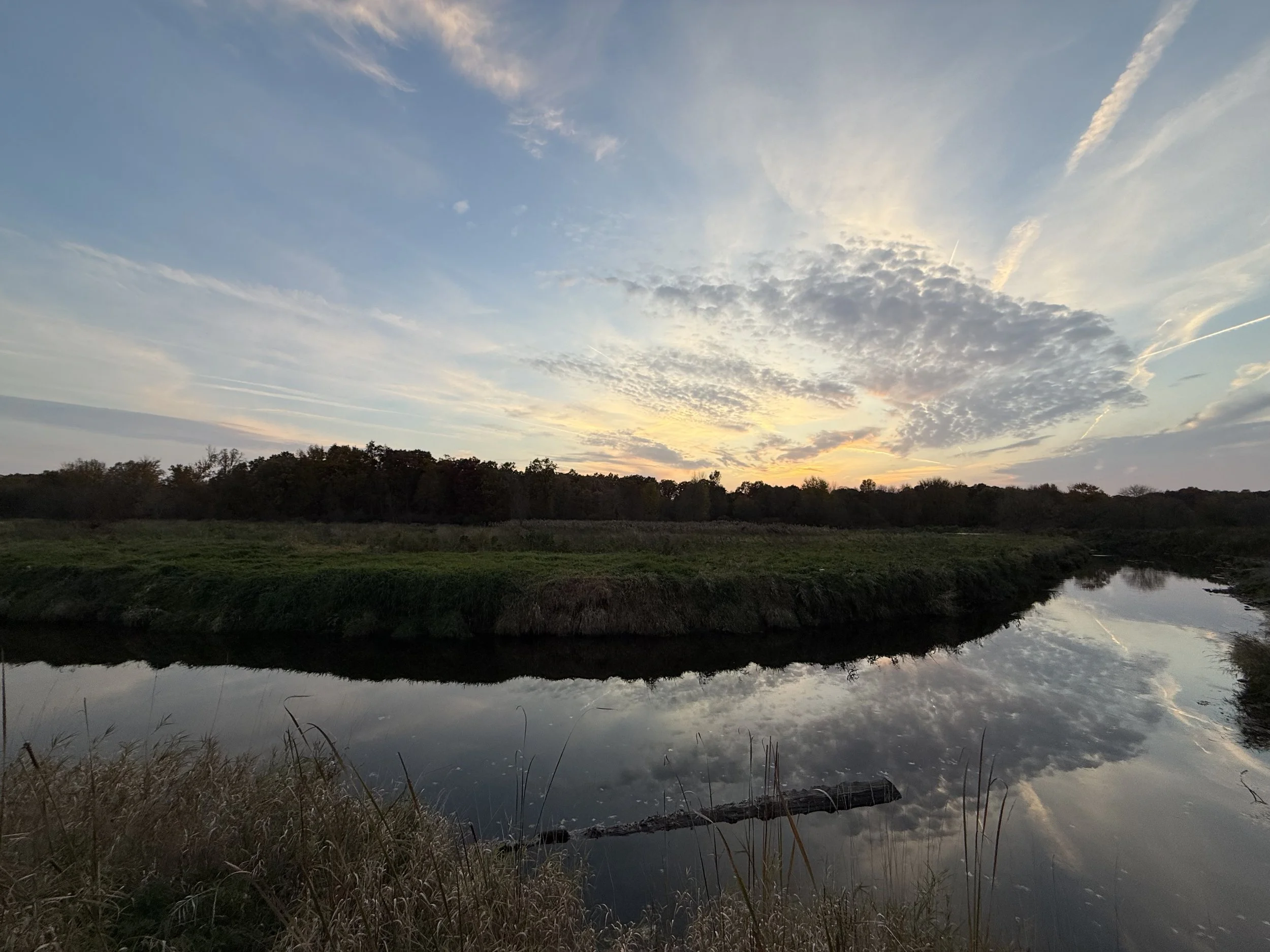 Sunset over grasslands and a creek under a dramtic October sky.