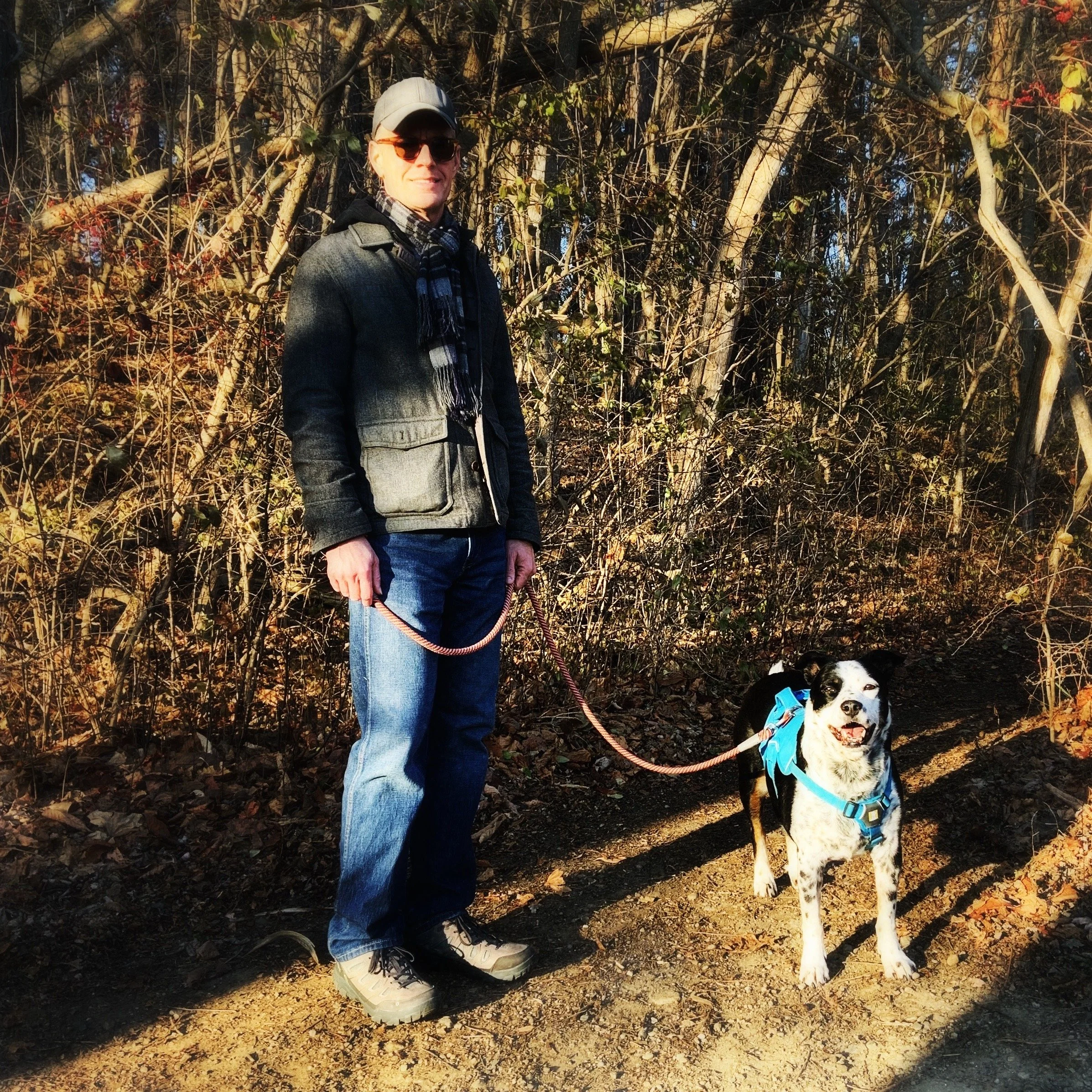 A black and white dog smiles on a path in the woods in winter with a person who loves him and looking at the person who loves him most.