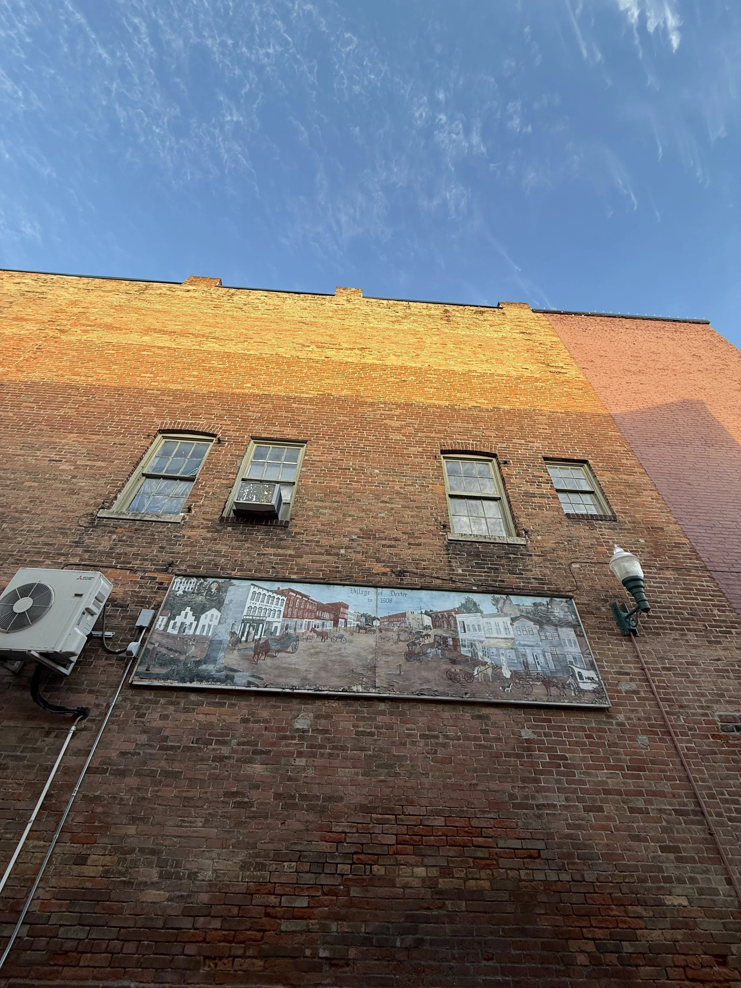 Morning sun on an old red brick building against a blue September sky with a mural painted on it in Dexter, Michigan.
