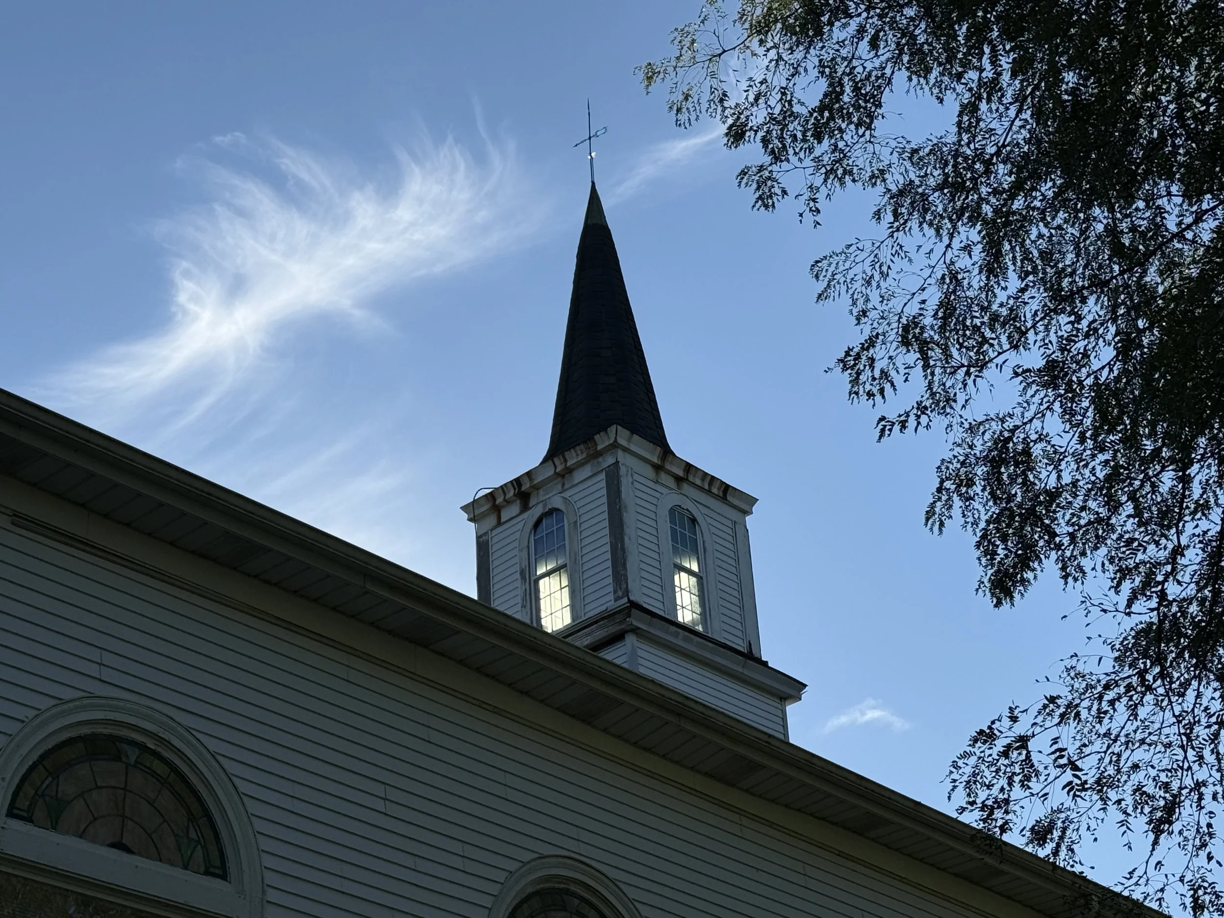 A church steeple lit with natural light against a blue sky in morning.